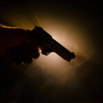 Silhouette of a hand holding a handgun against a dramatic light background