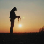 U.S. Food Prices Threatened: Fertilizer Crisis Unfolds Silhouette of a farmer holding soil against a sunset backdrop