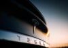 Close-up of a Tesla logo on a black car with a sunset in the background