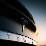 Close-up of a Tesla logo on a black car with a sunset in the background