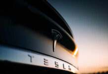 Close-up of a Tesla logo on a black car with a sunset in the background