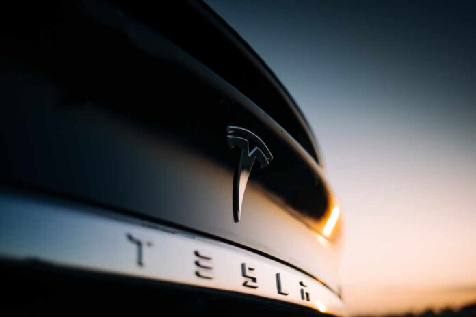Close-up of a Tesla logo on a black car with a sunset in the background