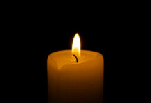 A lit candle with a soft flame against a black background