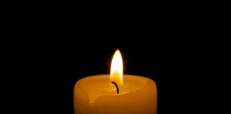 A lit candle with a soft flame against a black background