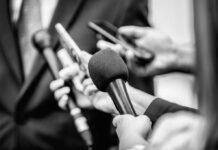 Close-up of microphones held by journalists during a press conference