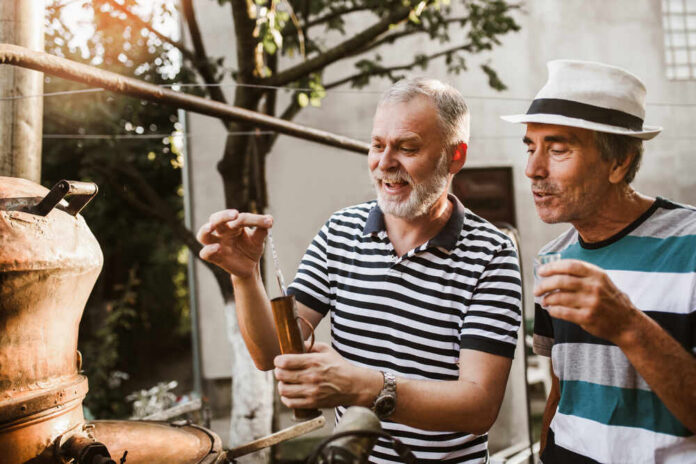 shutterstock_1822680428.jpg Two men engaged in a distillation process outdoors, examining a tool
