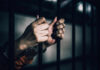 Hands gripping prison bars in a dimly lit environment
