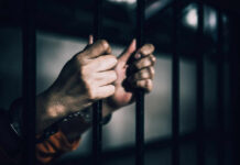 Hands gripping prison bars in a dimly lit environment