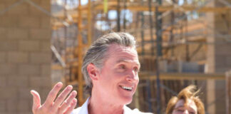 Gas Prices SOAR: California’s Homegrown Crisis? A man speaking at a construction site with a microphone, smiling, while a woman in the background laughs.