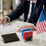 An official reviewing documents with a small American flag and stamps on the table