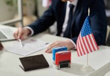 An official reviewing documents with a small American flag and stamps on the table
