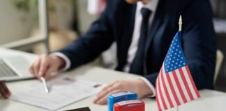 An official reviewing documents with a small American flag and stamps on the table