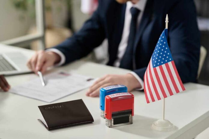 An official reviewing documents with a small American flag and stamps on the table