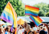 A hand holding rainbow flags at a pride event with a crowd in the background