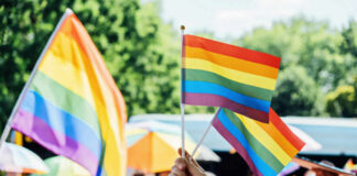 Flag Law Fallout: Boise’s Pride Flag Taken Down A hand holding rainbow flags at a pride event with a crowd in the background