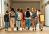A group of children walking together in a school hallway, each carrying a backpack
