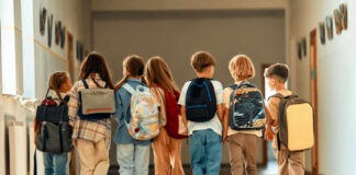 A group of children walking together in a school hallway, each carrying a backpack