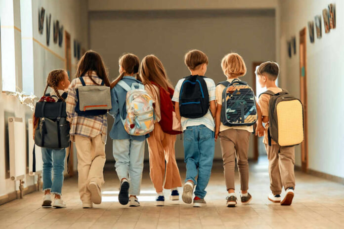 A group of children walking together in a school hallway, each carrying a backpack