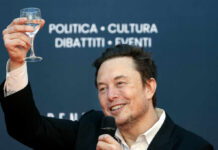 A man in a black suit raising a glass of water while smiling at an event