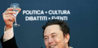 A man in a black suit raising a glass of water while smiling at an event
