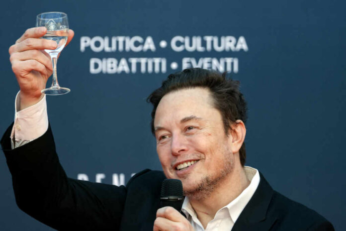 A man in a black suit raising a glass of water while smiling at an event