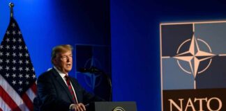 A man speaking at a podium with a NATO logo and an American flag in the background