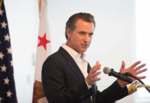 Massive Taxpayer Debacle — Rail to Nowhere A man in a suit speaking into a microphone with a California flag in the background