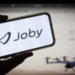 A hand holding a smartphone displaying the Joby logo