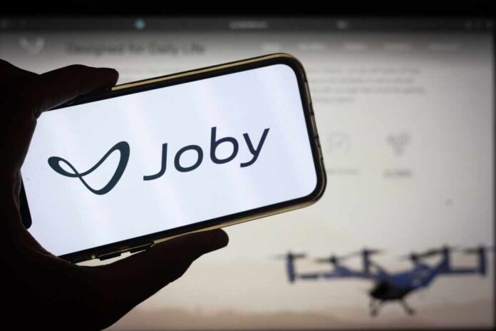 A hand holding a smartphone displaying the Joby logo