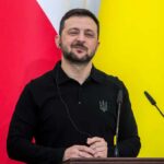 A political leader speaking at a press conference with flags in the background