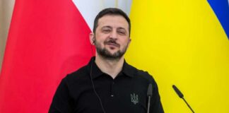 A political leader speaking at a press conference with flags in the background
