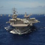 An aircraft carrier surrounded by various naval ships in the ocean