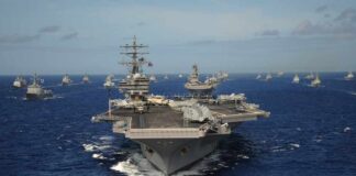 An aircraft carrier surrounded by various naval ships in the ocean