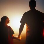 Silhouette of a parent and child wearing capes against a sunset