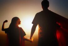 Silhouette of a parent and child wearing capes against a sunset