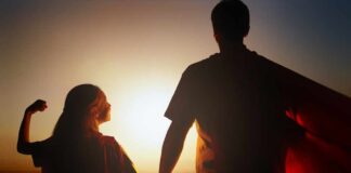 Silhouette of a parent and child wearing capes against a sunset