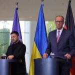 Two government officials at a press conference with flags in the background