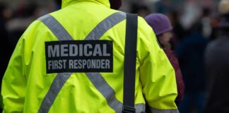 Medical first responder wearing a bright yellow jacket and carrying a red bag