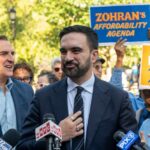 A politician speaking at a rally with supporters holding signs