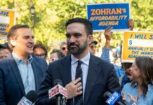 A politician speaking at a rally with supporters holding signs