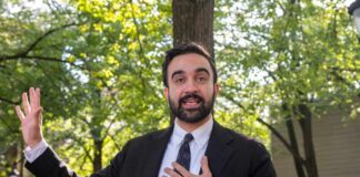 Man in a suit speaking outdoors with trees in the background