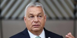 A government official speaking at a press conference with microphones in front