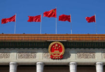 Chinese flags and national emblem displayed on a government building against a blue sky