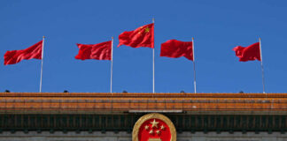 Chinese flags and national emblem displayed on a government building against a blue sky