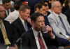 A man in a suit drinking water during a congressional hearing