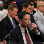 A man in a suit drinking water during a congressional hearing