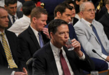 A man in a suit drinking water during a congressional hearing