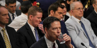 A man in a suit drinking water during a congressional hearing