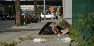A person lying on the sidewalk under a cardboard box in an urban setting