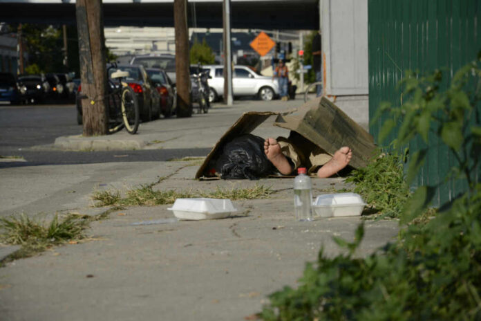 A person lying on the sidewalk under a cardboard box in an urban setting